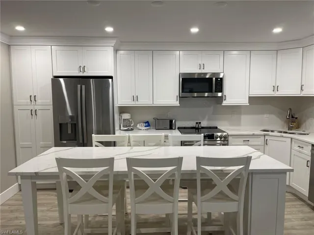 Kitchen featuring light wood-type flooring, a kitchen bar, backsplash, stainless steel appliances, and white cabinetry