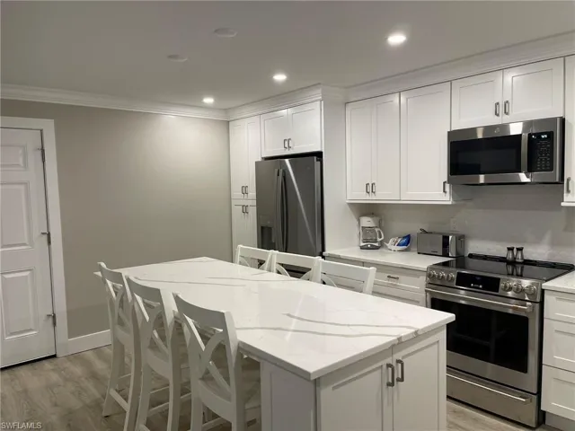 Kitchen with a breakfast bar, appliances with stainless steel finishes, white cabinets, light wood finished floors, and recessed lighting