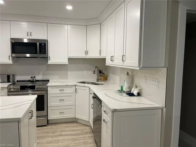Kitchen with appliances with stainless steel finishes, white cabinetry, backsplash, light stone countertops, and light wood-style flooring