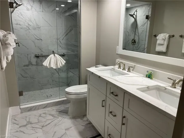 Full bathroom featuring a marble finish shower, light marble finish flooring, and double vanity