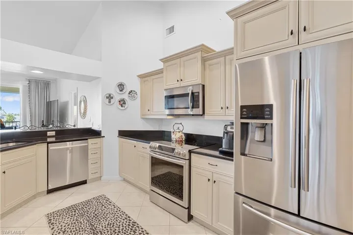 Kitchen featuring light tile patterned flooring, cream cabinetry, high vaulted ceiling, and appliances with stainless steel finishes