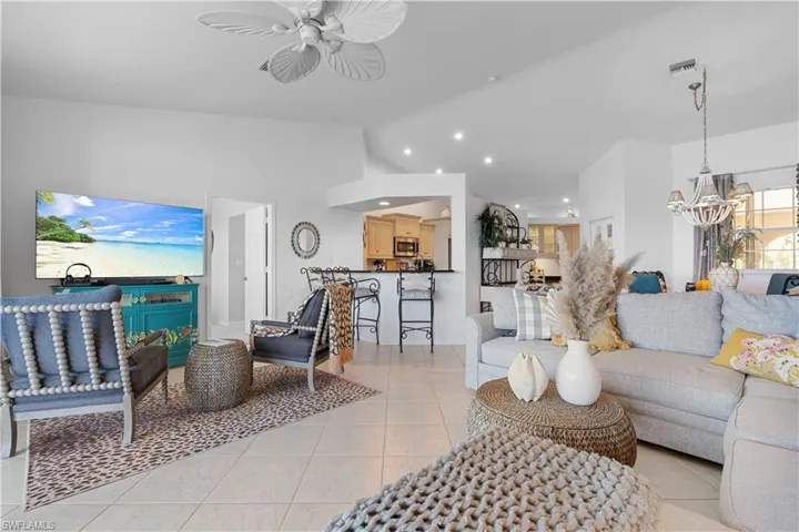 Tiled living room with ceiling fan with notable chandelier and high vaulted ceiling