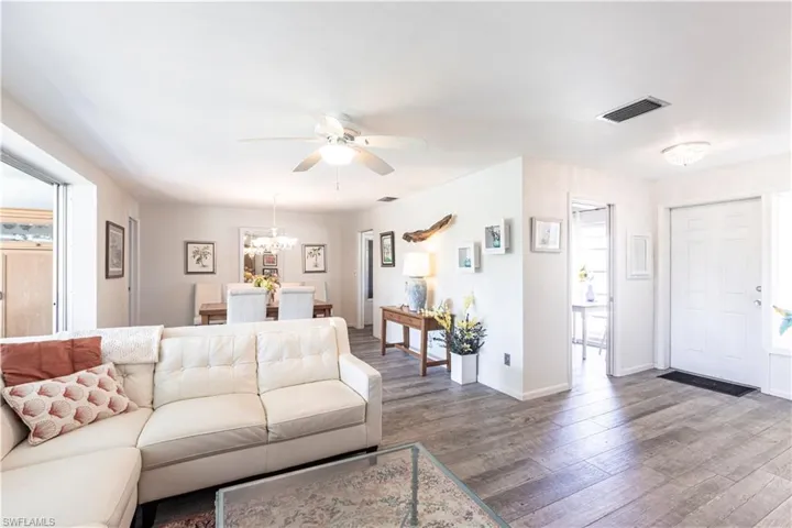 Open light filled Living room with ceiling fan with notable chandelier, wood finished floors, and baseboards