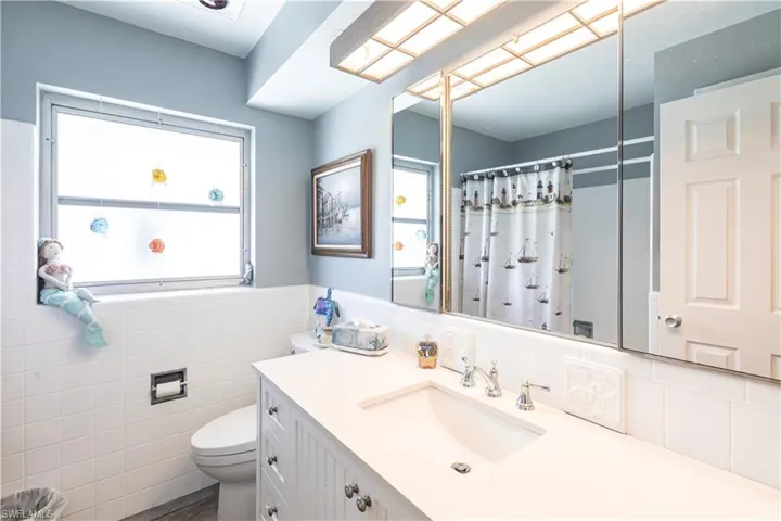 Guest Bathroom newly remolded with tile walls, toilet, a shower with shower curtain, wainscoting, and large vanity