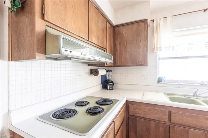 Kitchen with electric cooktop, exhaust hood,solid wood cabinetry, light countertops, and decorative backsplash