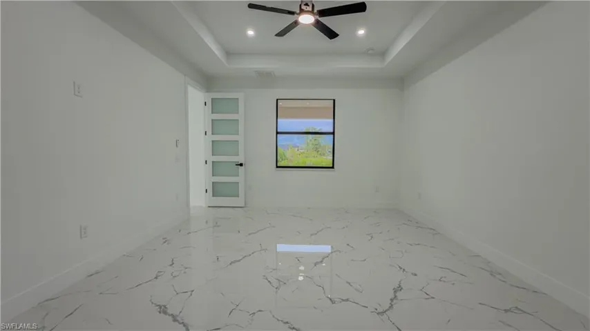 Empty room featuring a tray ceiling, recessed lighting, light marble finish floors, and ceiling fan