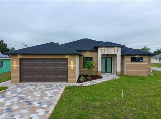 Prairie-style home with decorative driveway, an attached garage, a front yard, and stucco siding