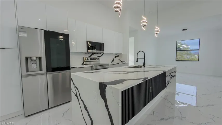 Kitchen with appliances with stainless steel finishes, modern cabinets, decorative light fixtures, white cabinetry, and light stone countertops