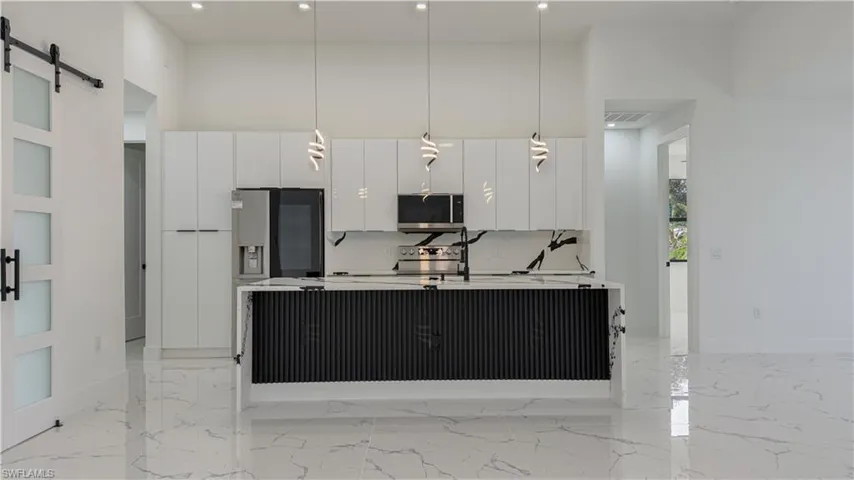 Kitchen with a barn door, modern cabinets, pendant lighting, white cabinetry, and a towering ceiling