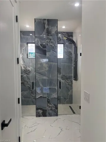 Bathroom with a marble finish shower and light marble finish flooring