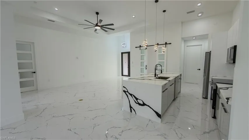 Kitchen featuring recessed lighting, light marble finish flooring, pendant lighting, a center island with sink, and stainless steel appliances