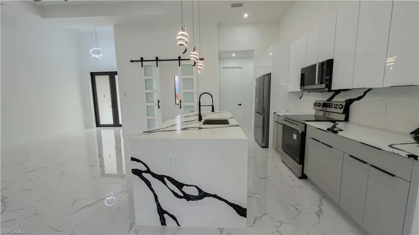 Kitchen featuring modern cabinets, appliances with stainless steel finishes, a barn door, decorative light fixtures, and a high ceiling