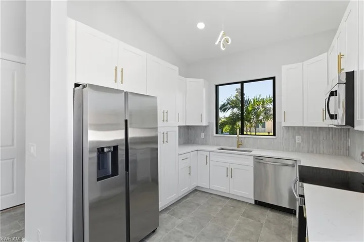 Kitchen with appliances with stainless steel finishes, white cabinets, lofted ceiling, light stone counters, and recessed lighting