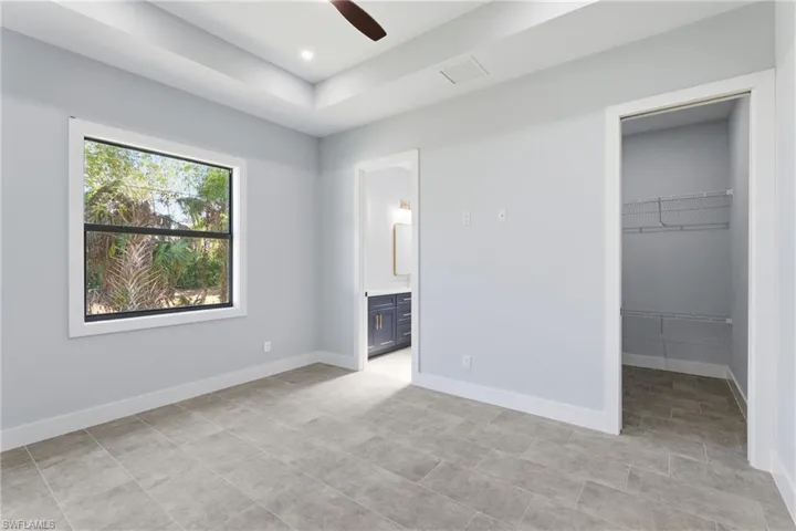 Unfurnished bedroom with ensuite bathroom, a spacious closet, a ceiling fan, and recessed lighting