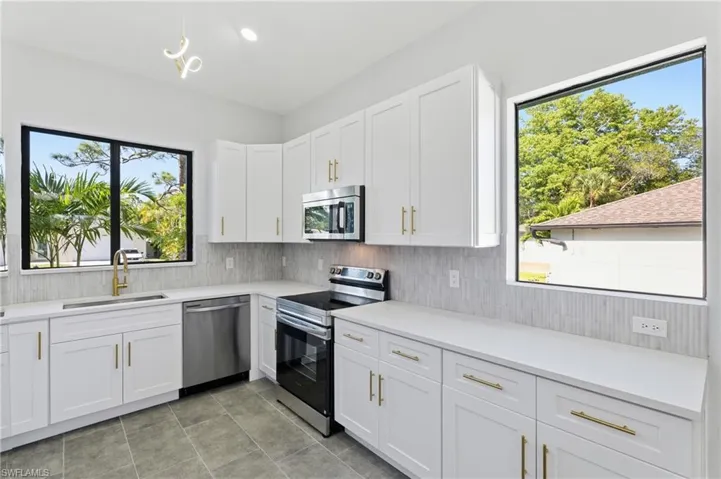 Kitchen with appliances with stainless steel finishes, white cabinets, light stone counters, recessed lighting, and decorative backsplash