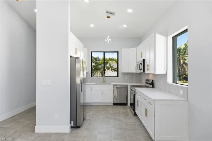 Kitchen with stainless steel appliances, white cabinets, decorative light fixtures, light stone countertops, and recessed lighting