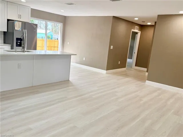Kitchen featuring stainless steel fridge with ice dispenser, light wood-type flooring, recessed lighting, light stone countertops, and white cabinets