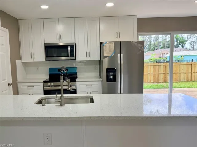 Kitchen featuring stainless steel appliances, light stone counters, white cabinets, recessed lighting, and tasteful backsplash
