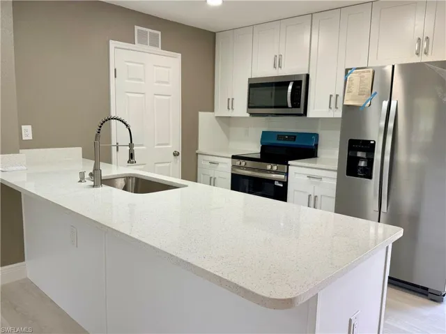 Kitchen featuring a peninsula, stainless steel appliances, white cabinets, light stone countertops, and light wood-style floors