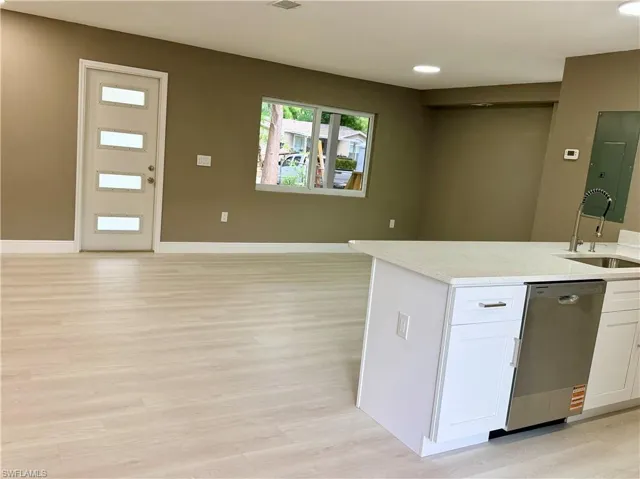 Kitchen featuring stainless steel dishwasher, light wood-style floors, light stone counters, electric panel, and open floor plan