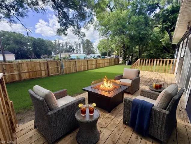 Expansive wooden deck featuring a built-in fire pit, surrounded by a manicured lawn and a privacy fence
