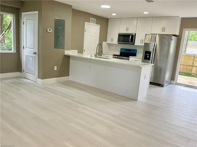 Kitchen featuring stainless steel appliances, a peninsula, electric panel, light wood-type flooring, and white cabinetry