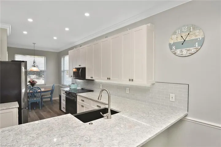 Kitchen featuring white cabinets, crown molding, black appliances, decorative light fixtures, and light stone counters