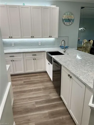 Kitchen with white cabinets, light wood finished floors, light stone counters, and tasteful backsplash