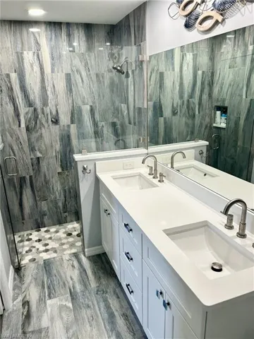 Bathroom featuring a stall shower, double vanity, tile walls, and wood finished floors