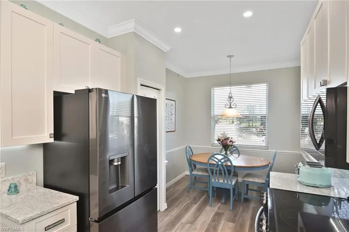 Kitchen with white cabinetry, stainless steel refrigerator with ice dispenser, black electric range oven, crown molding, and decorative light fixtures