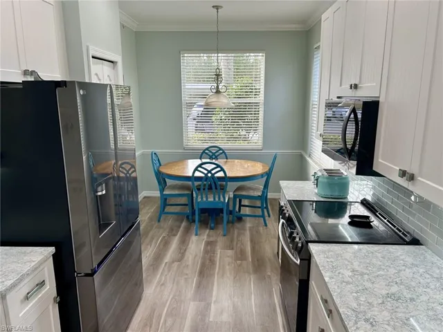 Kitchen with stainless steel appliances, white cabinets, ornamental molding, light stone counters, and decorative light fixtures