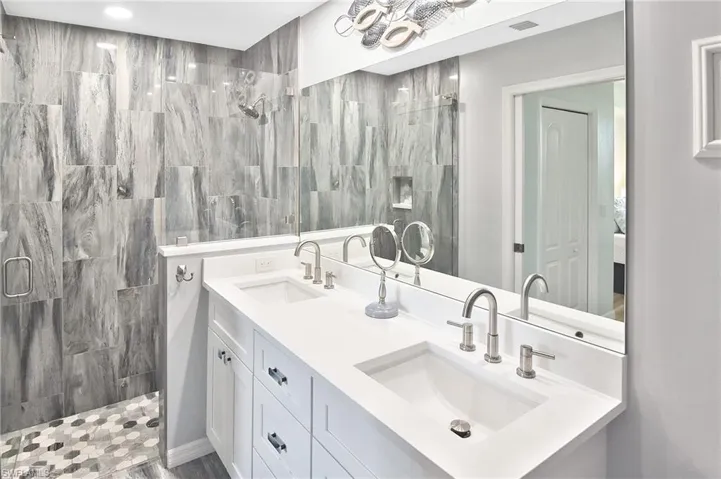 Full bath featuring double vanity, a stall shower, and tile walls