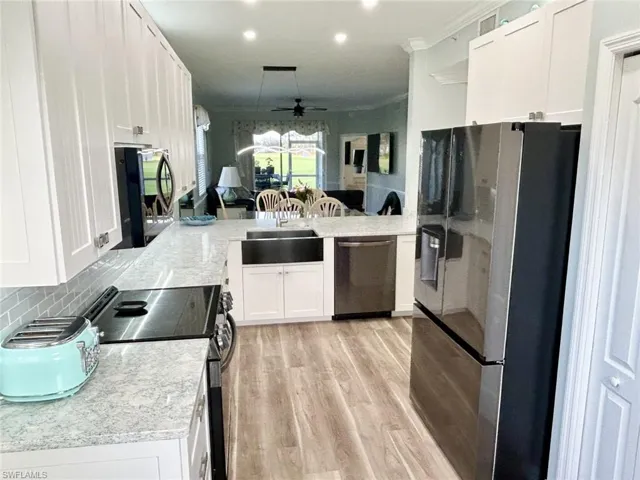 Kitchen with white cabinets, appliances with stainless steel finishes, light wood-style flooring, ceiling fan, and pendant lighting