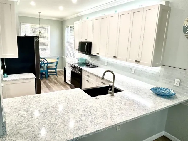 Kitchen with white cabinetry, black range with electric stovetop, light stone counters, tasteful backsplash, and freestanding refrigerator