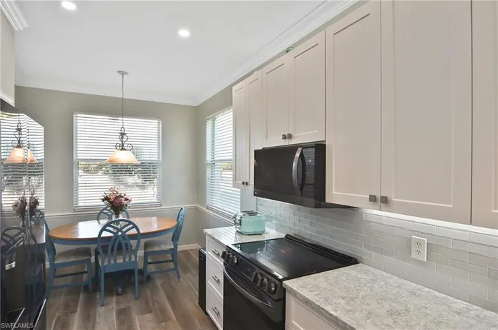 Kitchen featuring black appliances, pendant lighting, crown molding, white cabinetry, and dark wood-style flooring