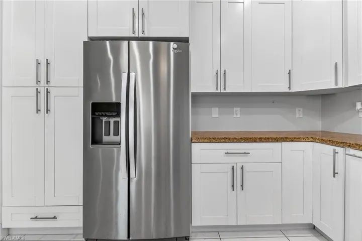 Kitchen with stainless steel refrigerator with ice dispenser, white cabinetry, and dark stone countertops