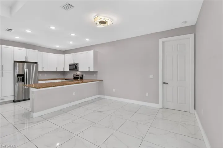 Kitchen featuring stainless steel appliances, a peninsula, dark stone countertops, white cabinets, and light marble finish floors