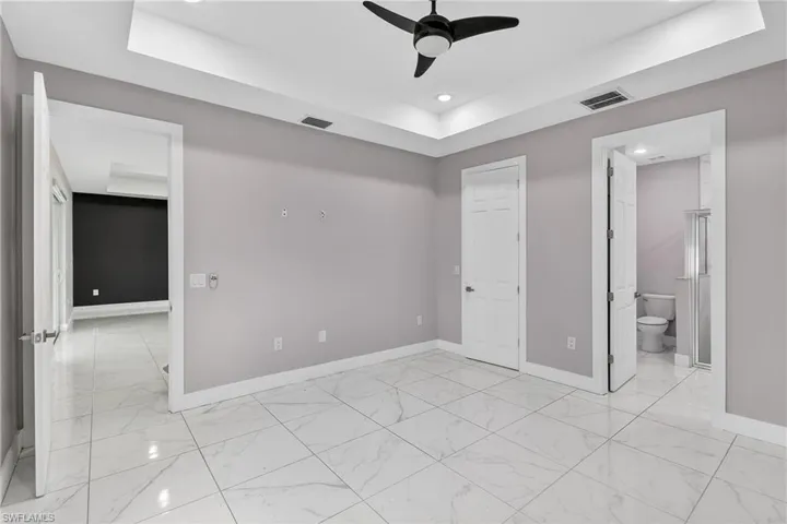Unfurnished bedroom featuring a tray ceiling, a ceiling fan, recessed lighting, and ensuite bath