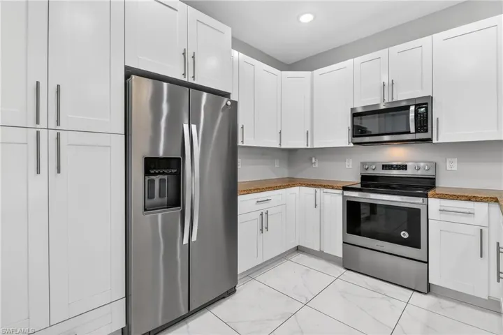 Kitchen with stainless steel appliances, white cabinets, light marble finish flooring, and recessed lighting