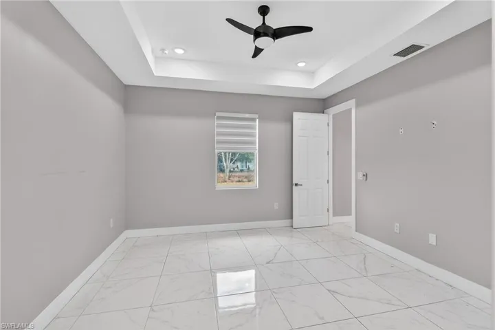 Unfurnished room featuring a raised ceiling, a ceiling fan, light marble finish flooring, and recessed lighting