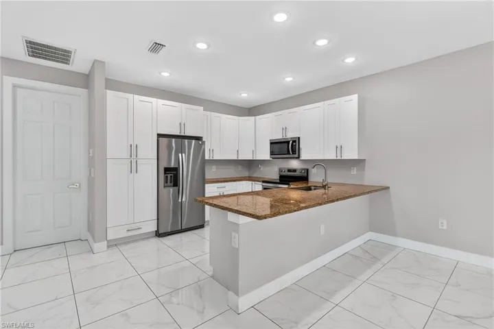 Kitchen with stainless steel appliances, dark stone countertops, light marble finish flooring, a peninsula, and recessed lighting