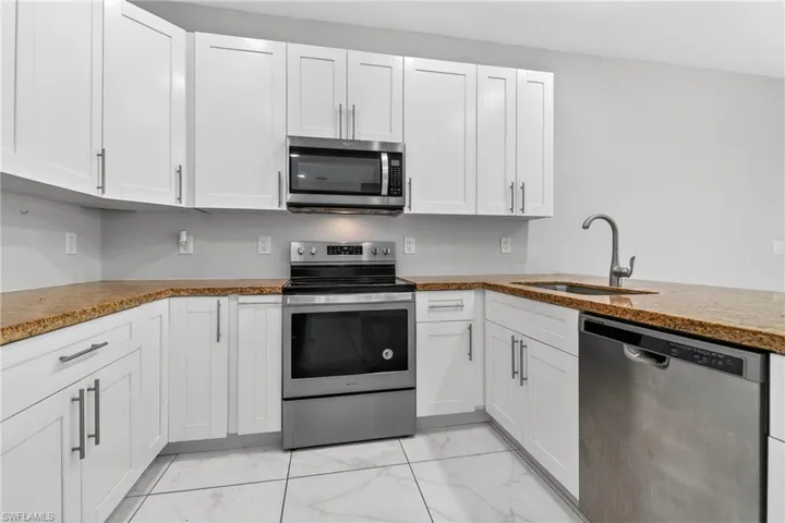 Kitchen with stainless steel appliances, white cabinets, and light stone countertops