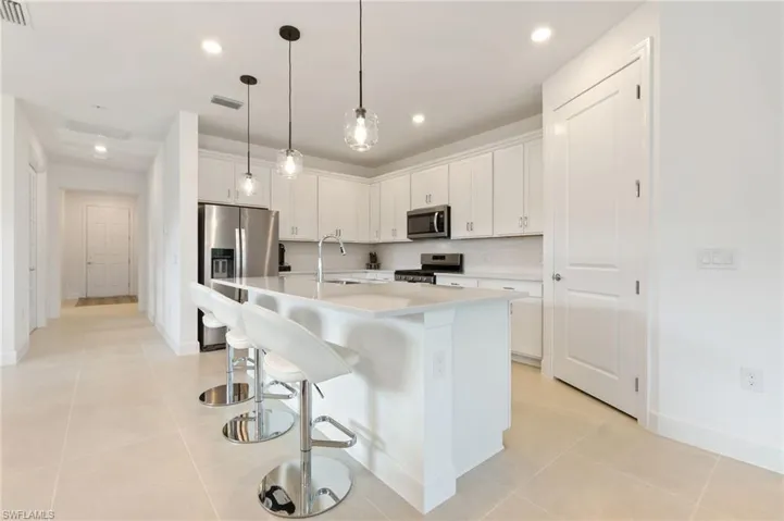 Kitchen with a breakfast bar area, a center island with sink, white cabinets, decorative light fixtures, and stainless steel appliances