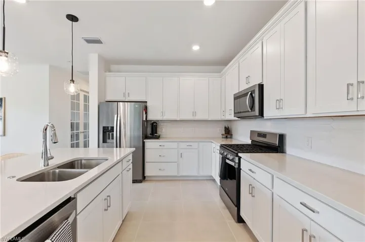 Kitchen featuring appliances with stainless steel finishes, decorative light fixtures, white cabinets, light stone countertops, and recessed lighting