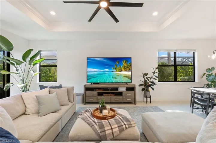 Living room featuring a tray ceiling, a ceiling fan, recessed lighting, ornamental molding, and a chandelier
