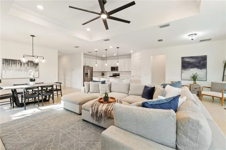 Living area with a tray ceiling, light tile patterned floors, recessed lighting, a chandelier, and a ceiling fan