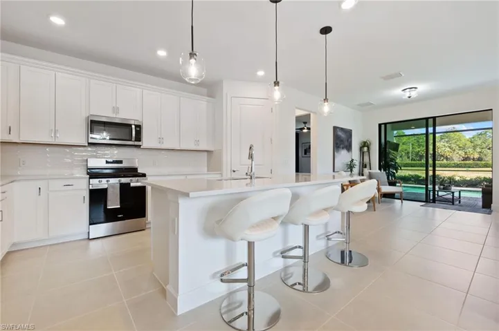 Kitchen featuring appliances with stainless steel finishes, decorative backsplash, white cabinets, a kitchen breakfast bar, and decorative light fixtures