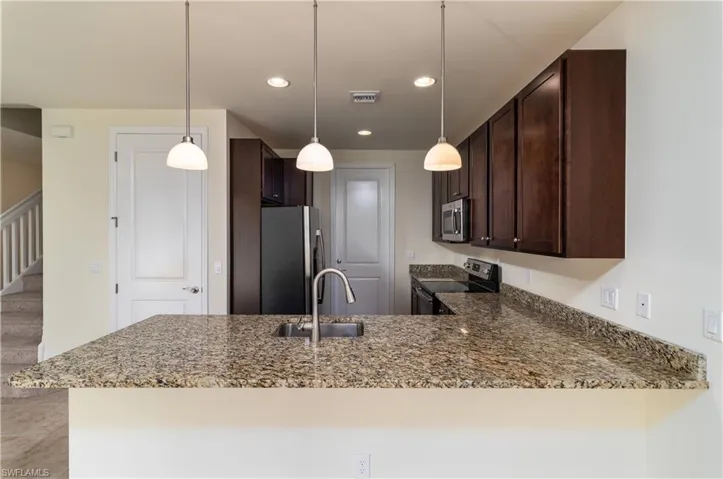 Kitchen featuring decorative light fixtures, dark stone counters, dark brown cabinets, and stainless steel appliances