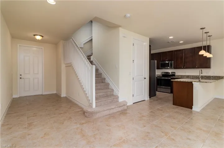 Kitchen with stainless steel appliances, light tile flooring, light stone counters, hanging light fixtures, and a breakfast bar