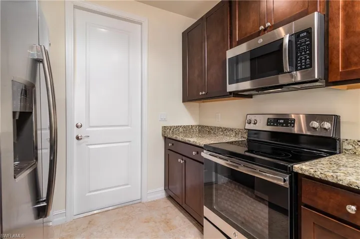 Kitchen featuring stainless steel appliances, light stone counters, dark brown cabinets, and light tile flooring